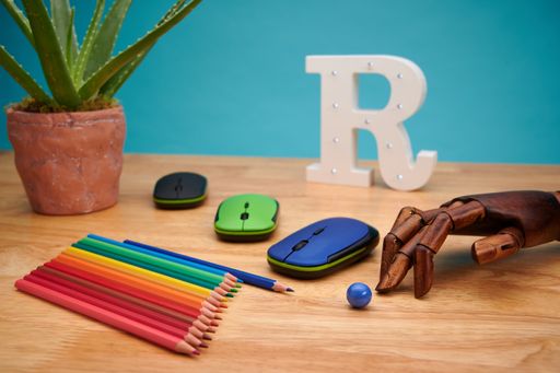 A selective focus shot of computer mouses with multicolored pencils, articulated wooden hand, and aloe plant on a wooden table