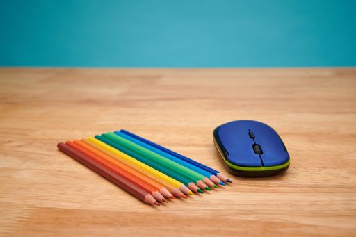 A closeup of a computer mouse and multicolored pencils on a wooden table