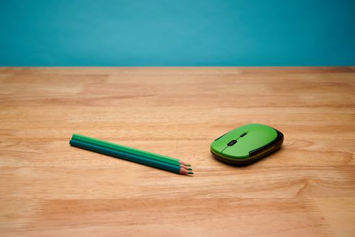 A closeup of a computer mouse and green pencils on a wooden desk