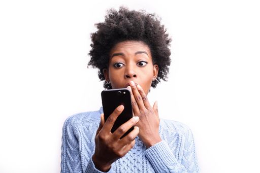A young black female looking surprised with her black phone isolated on a white background