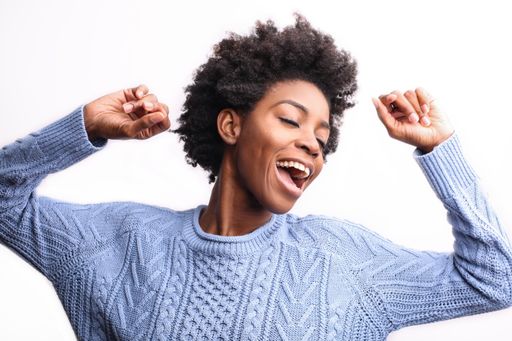 A young black female with a light blue sweater dancing happily isolated on a white background