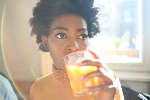 A young black female with curly black hair drinking orange juice indoors
