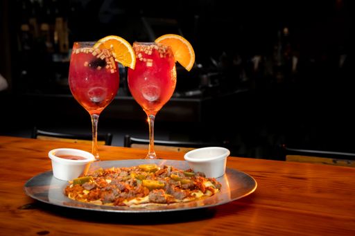 A selective focus shot of two Clericot cocktails with orange slices and pizza on wooden table