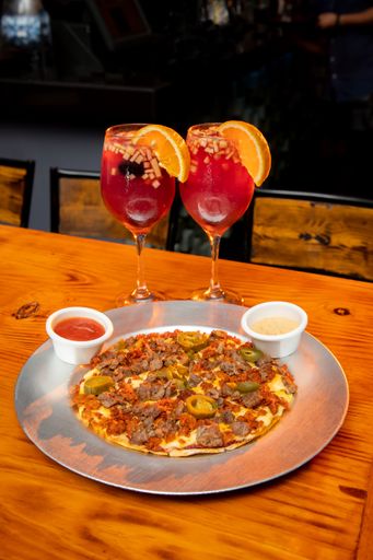 A selective focus shot of two Clericot cocktails with orange slices and pizza on a wooden table