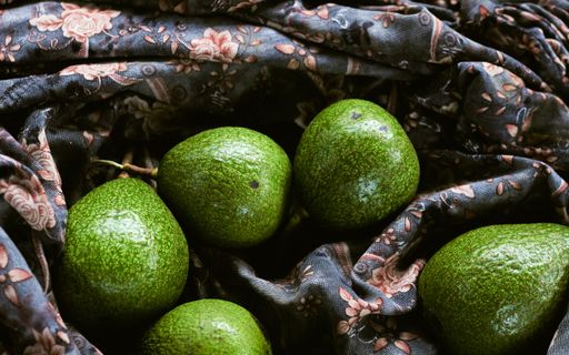A top view closeup of ripe avocados placed on a black cloth with a colorful flower on it