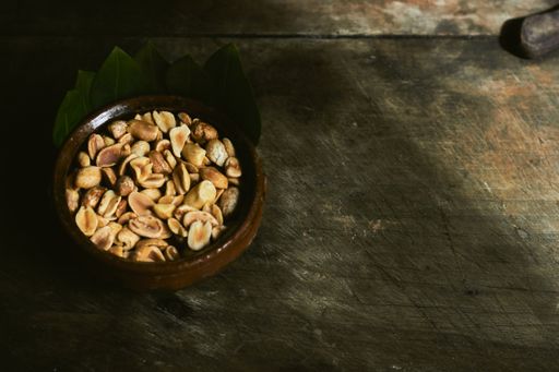 A top view closeup of pistachios inside of a brown ceramic bowl on a wooden table
