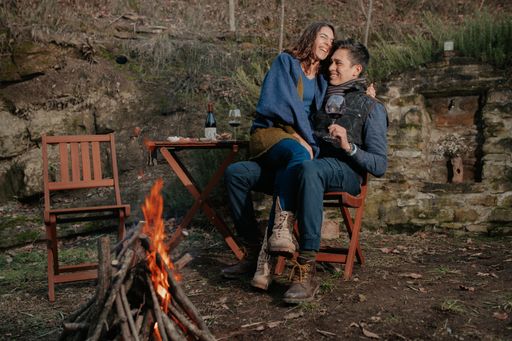 A loving happy couple after having a romantic picnic sitting near fire hugging each other and enjoying wine in nature