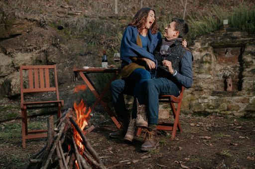 A loving happy couple after having a romantic picnic sitting near fire hugging each other and enjoying wine in nature