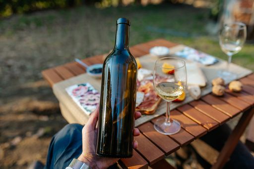 A hand holding a bottle of wine near a table set with appetizers and tasty food