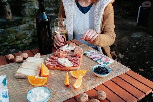 A girl sitting near a picnic table full of tasty appetizers and  holding a glass of white wine