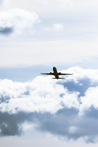 A vertical shot of a plane flying under a cloudy sky and sunlight at daytime