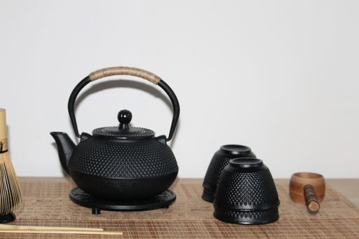 A closeup shot of a cast-iron Japanese teapot, teacups and wooden ladle