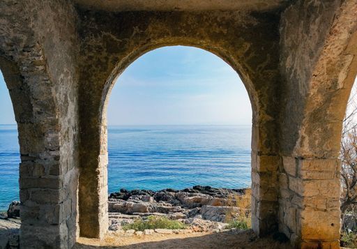 A beautiful view to the calm sea through an arch in a stone wall