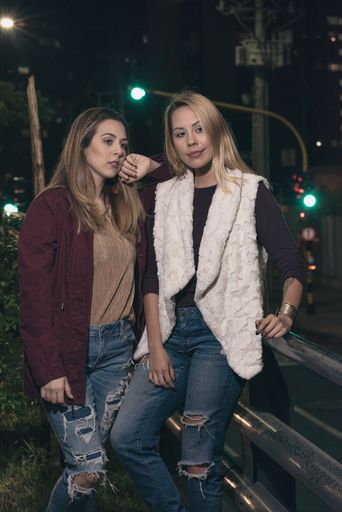 A vertical shot of two attractive Hispanic females posing in front of a camera on the street