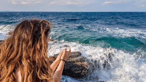 A closeup shot of a female sitting on a rocky seashore and observing a beautiful view of raging waves