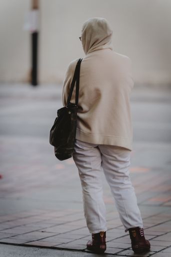 A view of a woman hearing a hijab standing with her back facing the camera in the street