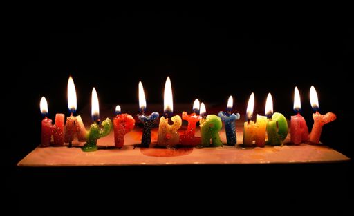 A closeup shot of Happy Birthday candles on a cake with a dark background