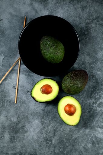A fresh ripe Hass avocado on a dark bowl and gray ceramic tile surface