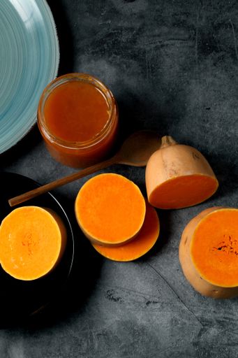 A vertical top view of sliced butternut squash with a jar of pumpkin jam on a dark ceramic surface
