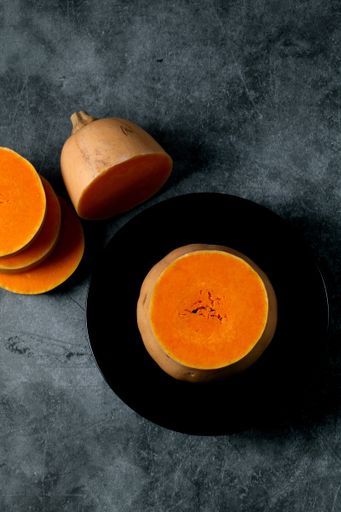 A vertical top view of sliced butternut squash on a dark bowl isolated dark-gray ceramic surface