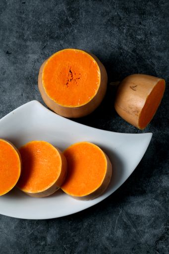 A vertical top view of sliced butternut squash on a white platter isolated dark-gray ceramic surface