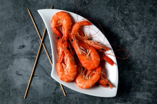 A top view of cooked shrimp on a white platter with sticks on a gray ceramic surface