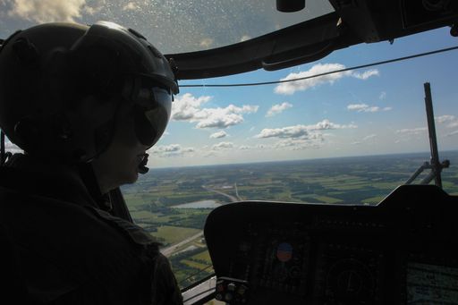 Helicopter pilot in cockpit flying over green Danish landscape under a nice blue skye whit white clouds. Wearing cool helmet.