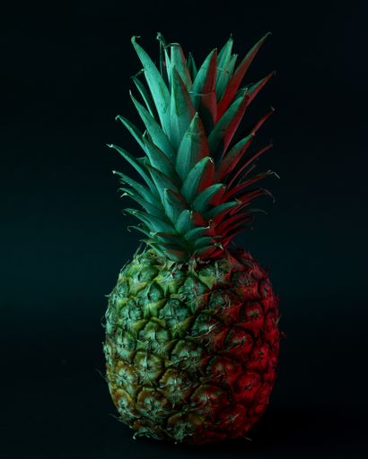 A vertical shot of a Ripe pineapple with green lighting on a black background