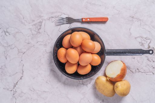 A top view of fresh organic eggs in a pan with an onion and potatoes on table