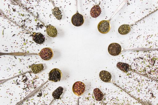 A top view of vintage silverware spoons with dry tea leaves arrange in a circle on a white background