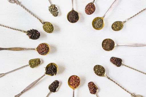 A top view of vintage silverware spoons with dry tea leaves arranged in a circle on a white background