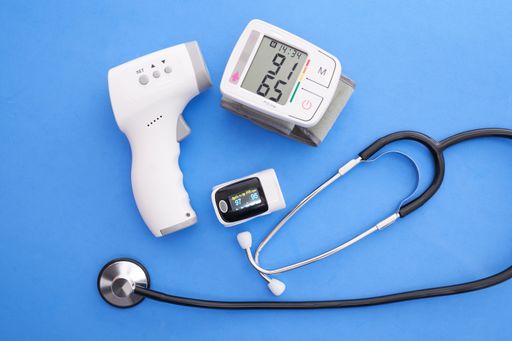 A blood pressure monitor, oximeter, digital thermometer and stethoscope on blue background