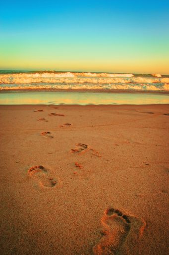 A vertical shot of human footprints on a wet sandy beach with a beautiful wavy seascape view