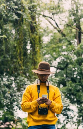 Young man traveler in a green forest, checking his mobile phone. communication concept.