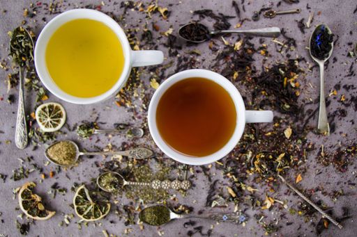 A flat lay composition with two cups of natural and herbal tea and vintage silverware spoons with an assortment of dry tea leaves