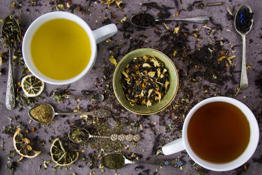 A flat lay composition with two cups of natural and herbal tea and vintage silverware spoons with an assortment of dry tea leaves