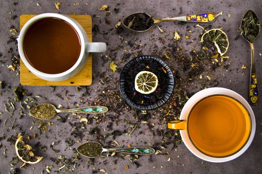 A top view of natural herbal teacups with assorted dried tea leaves and a collection of vintage spoons
