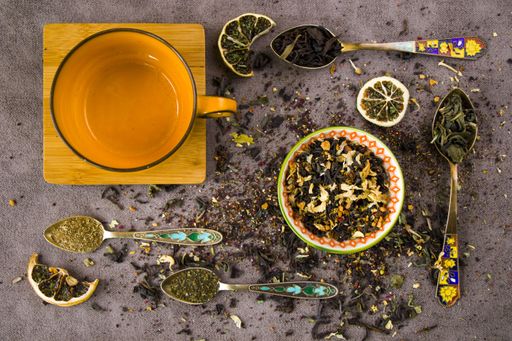 A flat lay composition with an empty mug and vintage silverware spoons with an assortment of dry tea leaves