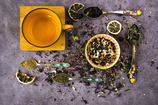 A top view of natural herbal teacups with assorted dried tea leaves and a collection of vintage spoons