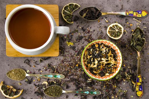 A top view of natural herbal teacups with assorted dried tea leaves and a collection of vintage spoons