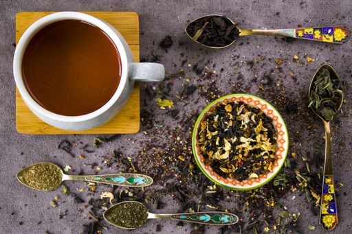 A flat lay composition with a cup of black tea and vintage silverware spoons with an assortment of dry tea leaves