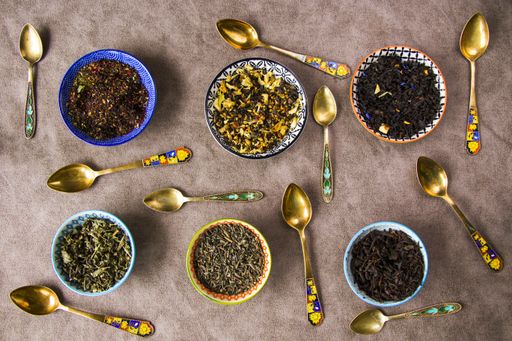 A top view of herbal and natural dry tea set in colorful small bowls and vintage silverware spoons