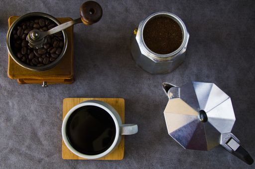 A top view of a coffee maker, grinder, and a cup of coffee on a gray background