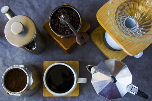 A top view of coffee makers, grinder, and a cup of coffee on a gray background
