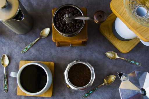A top view of coffee makers, grinder, and a cup of coffee on a gray background
