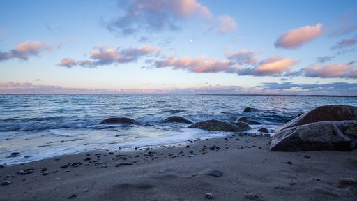 A calm empty sand beach with big rocks at sunset