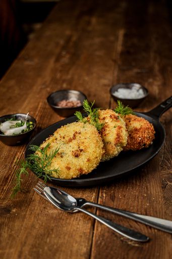 A vertical shot of delicious cutlets on a pan with greenery on the wooden table