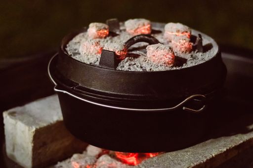 A black dutch oven with red glowing coal on it and underneath.