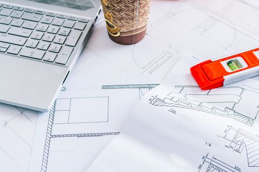 A top view of blueprints, balance ruler, laptop, and a cup of coffee on a desk