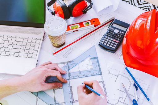 Architect hand holding pencil working with laptop and blueprints for architectural plan, engineer sketching a construction project concept.